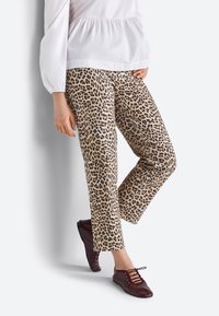 Luipaardprint, beige broek met een rechte snit en slim fit, gedragen met een wit topje en bordeauxrode veterschoenen, tegen een lichte achtergrond.