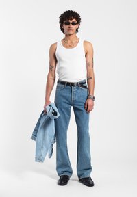 Valkoinen ribattu toppi, siniset levenevät farkut, vaaleansininen farkkutakki kädessä, käytetyt mustat kengät ja pienet mustat aurinkolasit.