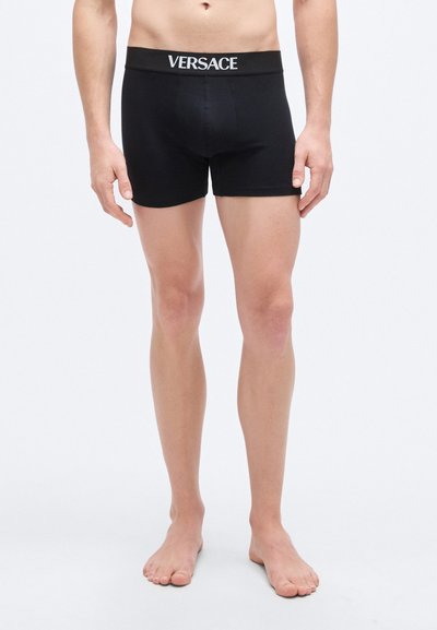 Boxer en coton noir avec une ceinture élastique de marque. Texture lisse et coupe ajustée, doté d'une poche frontale pour un soutien optimal.