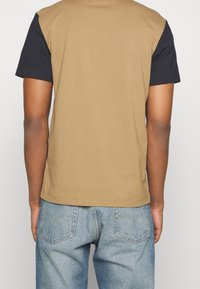 Short-sleeve T-shirt with a brown body and black sleeves, made of cotton, featuring a crew neckline and straight hem, worn with blue jeans.