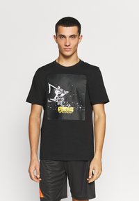 Sort bomuld t-shirt med grafisk print af en basketballscene med gul tekst. Kortærmet og design med rund hals.