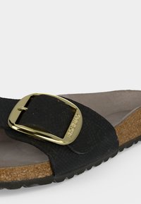 Μαύρο σανδάλι Birkenstock με μεγάλο χρυσό αγκράφα, φελλό πάτο και μορφοποιημένο μπεζ εσωτερικό πάτο.