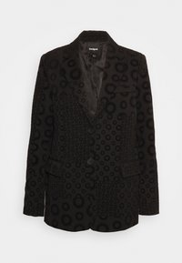 Blazer noir avec un motif texturé de motifs circulaires. Comprend deux boutons, une poche poitrine unique, et une doublure intérieure en satin.