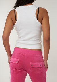 Canotta di cotone bianca con un design aderente, abbinata a pantaloni in velluto rosa con tasche posteriori e dettagli a pressione.