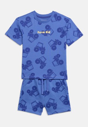 Ensemble chemise à manches courtes et short bleu avec des imprimés de tracteurs bleu foncé et le texte jaune « Farm Kid » sur la poitrine de la chemise.