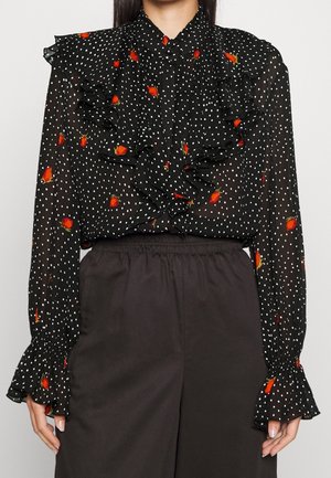 Zwarte doorzichtige blouse met witte stippen, verspreide rode rozenknoppen, gerimpeld voor en aan de manchetten, gecombineerd met een zwarte broek met hoge taille.