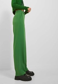 Groene wijde broek van een gladde stof, met een hoge taille, zijzakken en gedragen met stevige zwarte platform loafers.