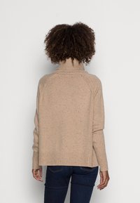 Vaaleanbeige neulepaita, jossa on korkea kaulus, ribbaatut hihansuut ja helma. Sen pintakuvio on kirjava ja se on rento malli raglan-hihoilla.