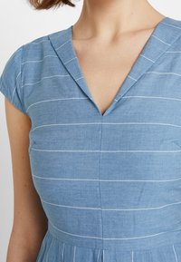 Blue chambray dress with white vertical stripes, featuring a V-neckline and short sleeves, smooth texture, and defined waistline.