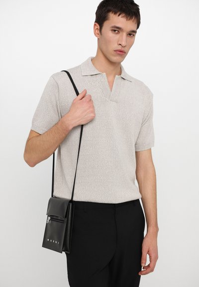 Svetlošedá pletená polo košeľa s golierom, skombinovaná s čiernymi nohavicami a malou čiernou crossbody taškou so zipsom a logom.