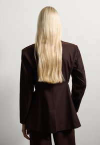 Brown tailored blazer met een getailleerde taille en lange mouwen, gecombineerd met bijpassende pantalons, gezien van achteren met lang, steil blond haar.