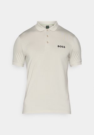 Lys beige polotrøye laget av glatt stoff, med krage, tre knapper og en subtil logo i svart på venstre bryst.