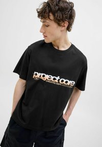 Zwart katoenen T-shirt met een geprinte logo in oranje en wit. Korte mouwen en een losse pasvorm met een ronde halslijn.