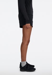 Pantalones cortos deportivos negros combinados con una camiseta de manga larga negra y zapatillas negras. Calcetines grises visibles sobre las zapatillas. Tela suave, ajuste casual.