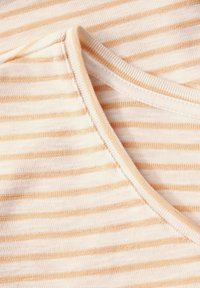 T-shirt med tynde, vandrette fersken- og crème-striber, rund udskæring og blødt, tekstureret stof. Synlige sømme som detaljer.
