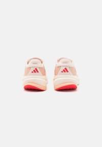 Sneakers Adidas z siateczkową cholewką w jasnoróżowym i kremowym kolorze. Posiadają gumową podeszwę z czerwonymi akcentami oraz logo trzech pasków na pięcie.