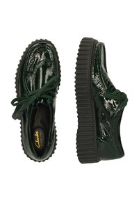 Zapatos con cordones de charol verde con una suela de goma negra robusta y cordones verdes a juego. Presentan una punta redondeada y una textura lisa.