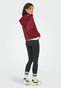 Burgundia lühike kapuutsiga sviiter, millel on nöör, koos mustade retuusidega, valgete triibuliste sokkidega ja turskete mustade ja valgete tennistega.