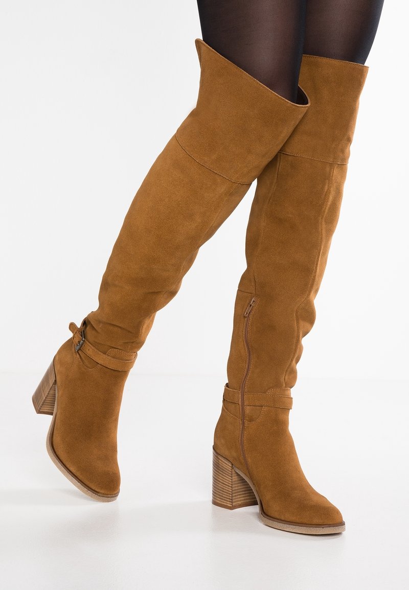 Hnědé semišové kozačky nad kolena se širokým ohybem, zipovým uzávěrem a detailem přezky. Blokový podpatek s jemnými vertikálními drážkami.