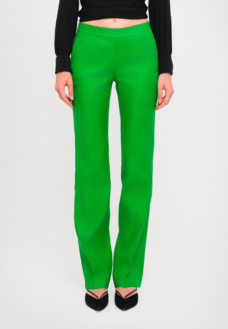 Pantalons verts ajustés avec une coupe droite, fabriqués en tissu lisse. Présentent une taille mi-haute et sont accompagnés de talons noirs.