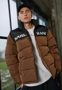 Rudas pūkinis švarkas su juodomis pečių dalimis, priekyje su baltu "KARL" logotipu. Lygus paviršius su siuvinėtu dizainu ir užtrauktuku.