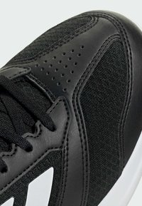 Schwarzer Sportsneaker mit einem strukturierten Obermaterial aus Stoff und glatten Lederakzenten, schwarzen Schnürsenkeln und einem weißen Logo-Detail.