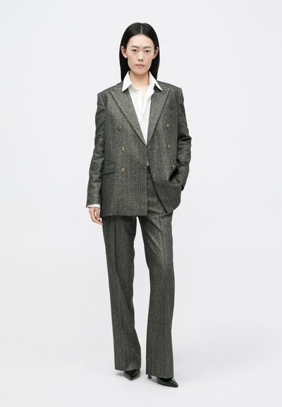 Pilkas dryžuotas dvigubo užsegimo švarkas su auksinėmis mygtukais, suderintas su atitinkamomis kelnių. Po juo balta marškinė su apykakle, aštrūs batai.