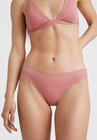 Šviesiai rožinis bikinių rinkinys, kuriame yra trikampio formos liemenėlė ir kelnaitės. Audinys lygus, su minimaliu siuvimu ir aerodinamine forma.