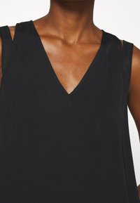 Top negro sin mangas con diseño de escote en V, fabricado en una tela suave, con tirantes mínimos y una textura lisa, que resalta una silueta simple y elegante.