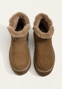 Hnedé semišové členkové topánky s mäkkým krémovým umelým kožuchom na golieri, zaoblenou špicou a šitými detailmi pozdĺž podrážky.