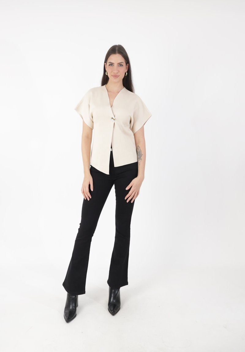Top beige de manga corta con escote en V y cierre de botones decorativos, combinado con pantalones de campana negros y botas negras hasta el tobillo.