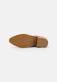 Chaussure pour femme avec une tige en suède synthétique beige, un bout rond et un talon bloc de hauteur moyenne. La semelle en caoutchouc présente un motif texturé pour une meilleure adhérence.
