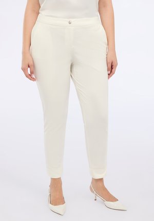 Pantaloni a gamba affusolata crema realizzati in tessuto morbido con chiusura a bottone, dotati di tasche laterali e risvolti. Abbinati a tacchi bianchi.