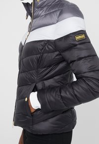 Puffer jacket featuring a color-block design in gray, white, and black. Made of shiny material with a zip closure and gold hardware accents.