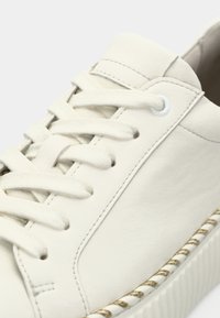 Fehér bőr sportcipő lekerekített orral, textil fűzőkkel és arany szövött díszítéssel a talpon. Sima textúra, minimális varrási részletekkel.