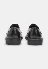 Chaussures habillées en cuir noir avec une finition lisse, bout rond, petit talon empilé et un minimum de détails de couture à l'arrière.