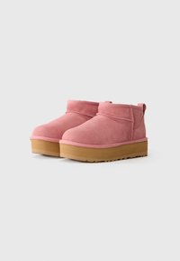 Une paire de bottines en suede rose avec de solides semelles en caoutchouc beige sur un fond blanc uni.