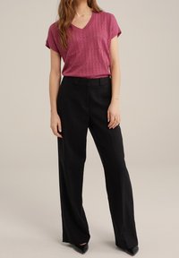 Růžový pletený top s výstřihem do V a krátkými rukávy, kombinovaný s černými kalhotami s vysokým pasem a širokými nohavicemi, s hladkou texturou a čistými liniemi.