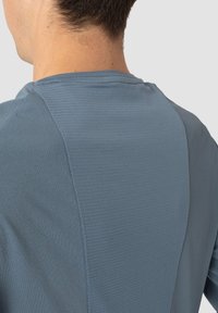 Lys blå treningsskjorte med et teksturert mesh-panel på ryggen, glatt hovedstoff og en moderne, tettsittende fasong.