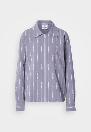 Camisa de manga larga gris claro con dobladillo recto, cremallera frontal y patrón repetido de logotipos blancos. Cuenta con cuello y puños con botones.