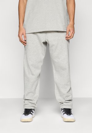 Gray jogger pants made of cotton blend fabric, featuring an elastic waistband and cuffs, paired with black and white athletic shoes.