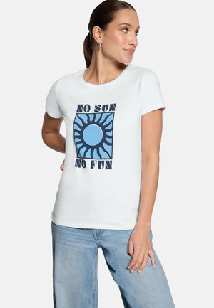 Femme avec queue de cheval portant un t-shirt blanc avec un motif de soleil bleu et le texte "Pas de soleil, pas de plaisir", associée à un jean bleu clair.