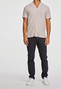 Short-sleeve light gray linen shirt with a notched collar, button front, paired with dark navy pants and white sneakers.