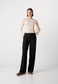 Stripete langermet topp i myk beige og hvit, sammen med høyhåndte svarte bukser. Tilbehøret inkluderer en beige veske og mørke sko.