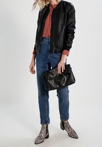 Veste bombardier en cuir noir, blouse rouille, jean bleu taille haute, sac à main noir avec quincaillerie circulaire, et bottines à imprimé léopard.