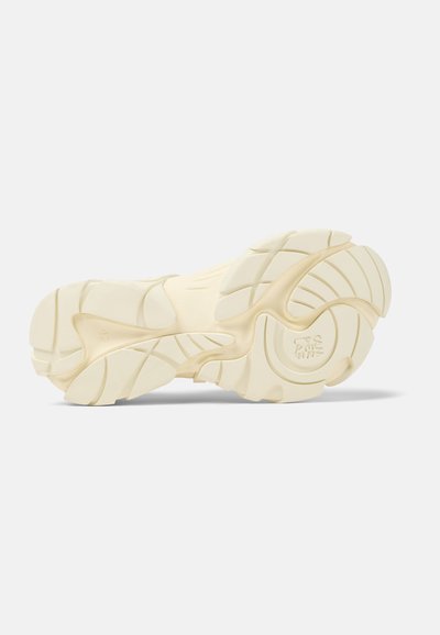 Sula av en sneakers, gjord av ljusfärgad gummi, med framträdande mönster och fåror, samt en cirkulär logotyp i mitten på undersidan.