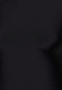 Chat noir aux yeux jaunes assis sur une surface sombre, regardant directement le spectateur.