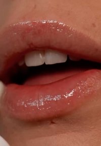 Lèvres roses pâles brillantes avec une texture lisse, légèrement ouvertes pour révéler des dents blanches. Des courbes subtiles soulignent la forme et l'éclat des lèvres.