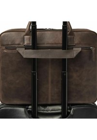 Malette en cuir marron attachée à la poignée déployée d'une valise noire à roulettes, avec des détails de fermeture éclair et une sangle en tissu pour bagages.