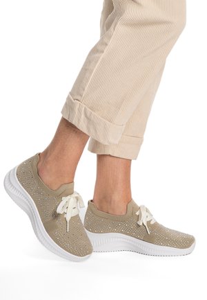 Beige Stricksneaker mit niedrigem Profil, weißer Sohle und Verzierungen aus kleinen Strasssteinen auf dem Obermaterial. Mit flachen weißen Schnürsenkeln geschnürt.
